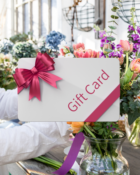 Someone arranges fresh flowers in a glass vase beside The Graceful Stem Gift Card, featuring a red ribbon and the words "Gift Card" on it.